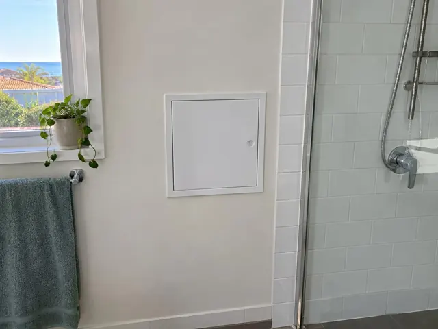 Small access panel in a painted bathroom wall beside a tiled shower and window in Bar Beach