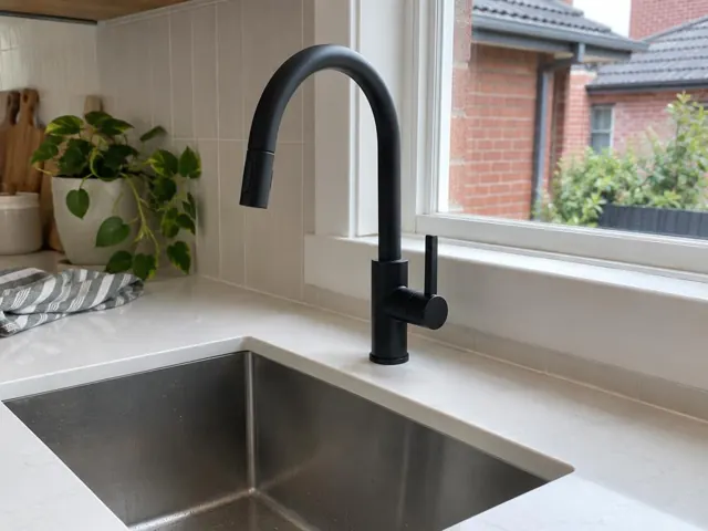 Black mixer tap above a stainless kitchen sink beside a window and tiled splashback in The Hill